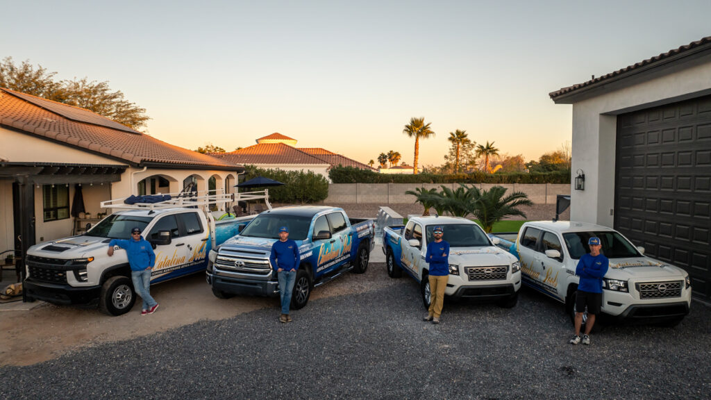 A fleet of Catalina Pools AZ trucks and workers proudly standing in front of them.